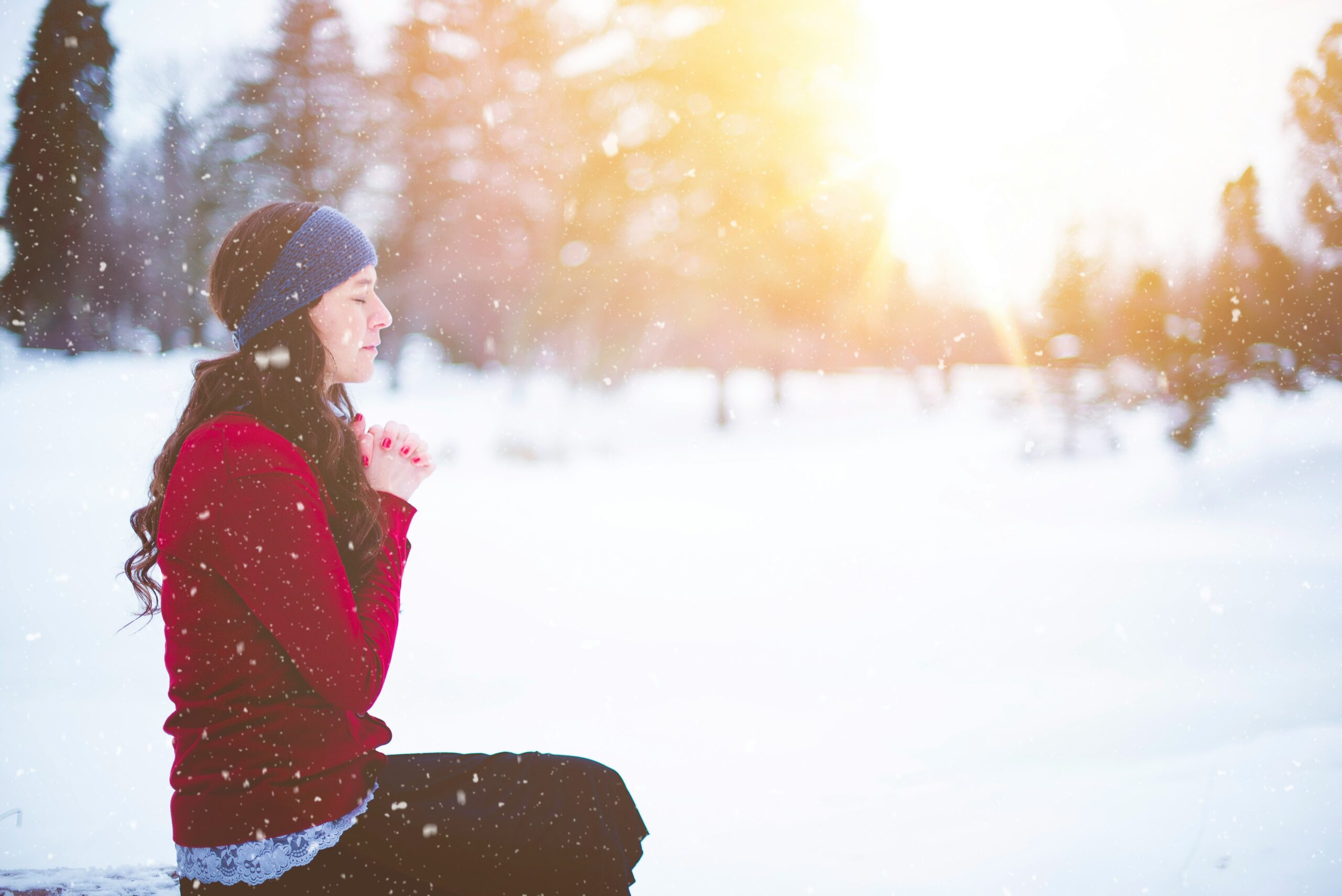 A woman meditates in the snow at sunset