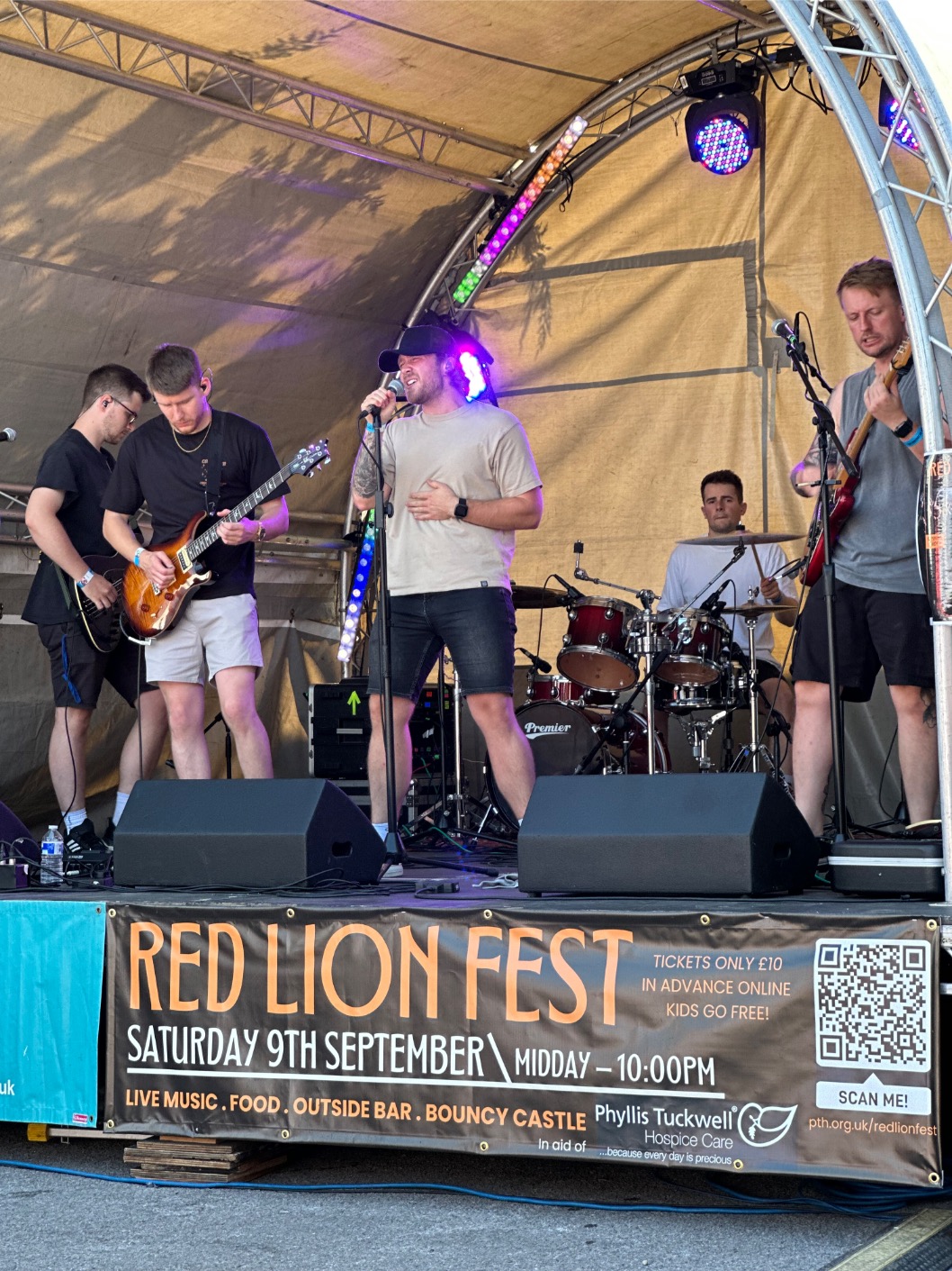 a band performs onstage with a large outdoor event banner advertising event details and fundraising ask 